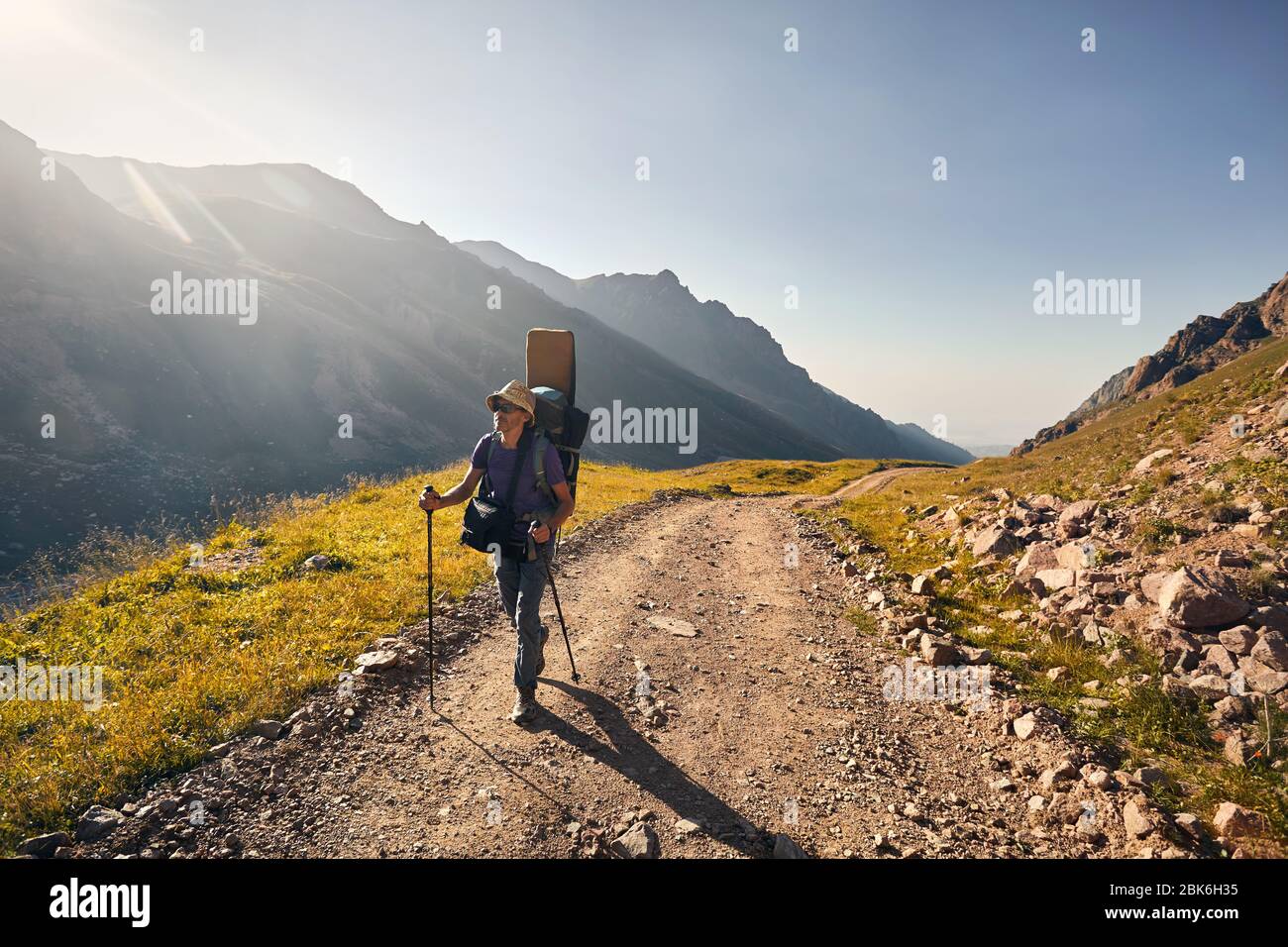 Excursionista con mochila grande es caminando por la carretera con espectaculares montañas en segundo plano Foto de stock