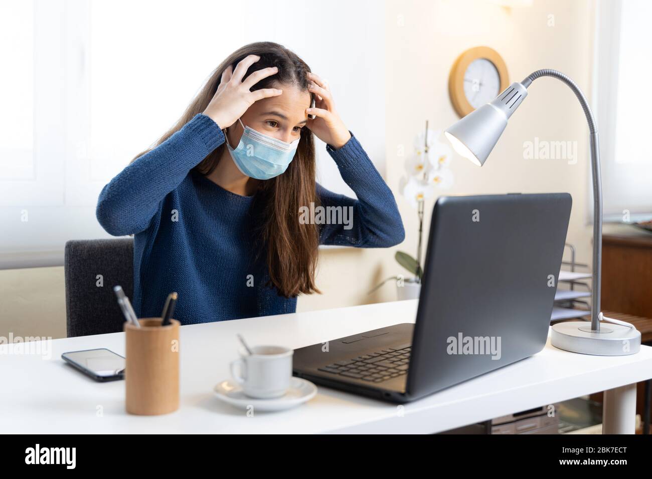 Un estudiante adolescente con máscara facial se queja de dolor de cabeza con la computadora en casa Foto de stock