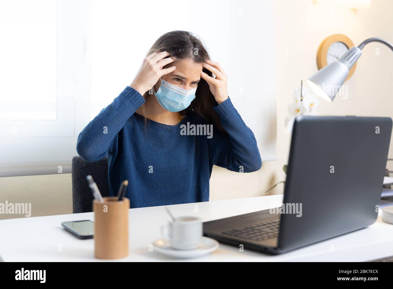 Un estudiante adolescente con máscara facial se queja de dolor de cabeza con la computadora en casa Foto de stock