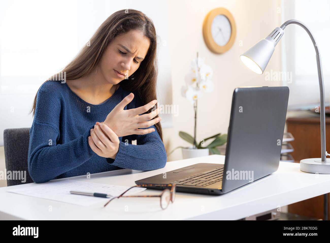 Niña adolescente con computadora portátil en casa quejándose de dolor en la muñeca Foto de stock