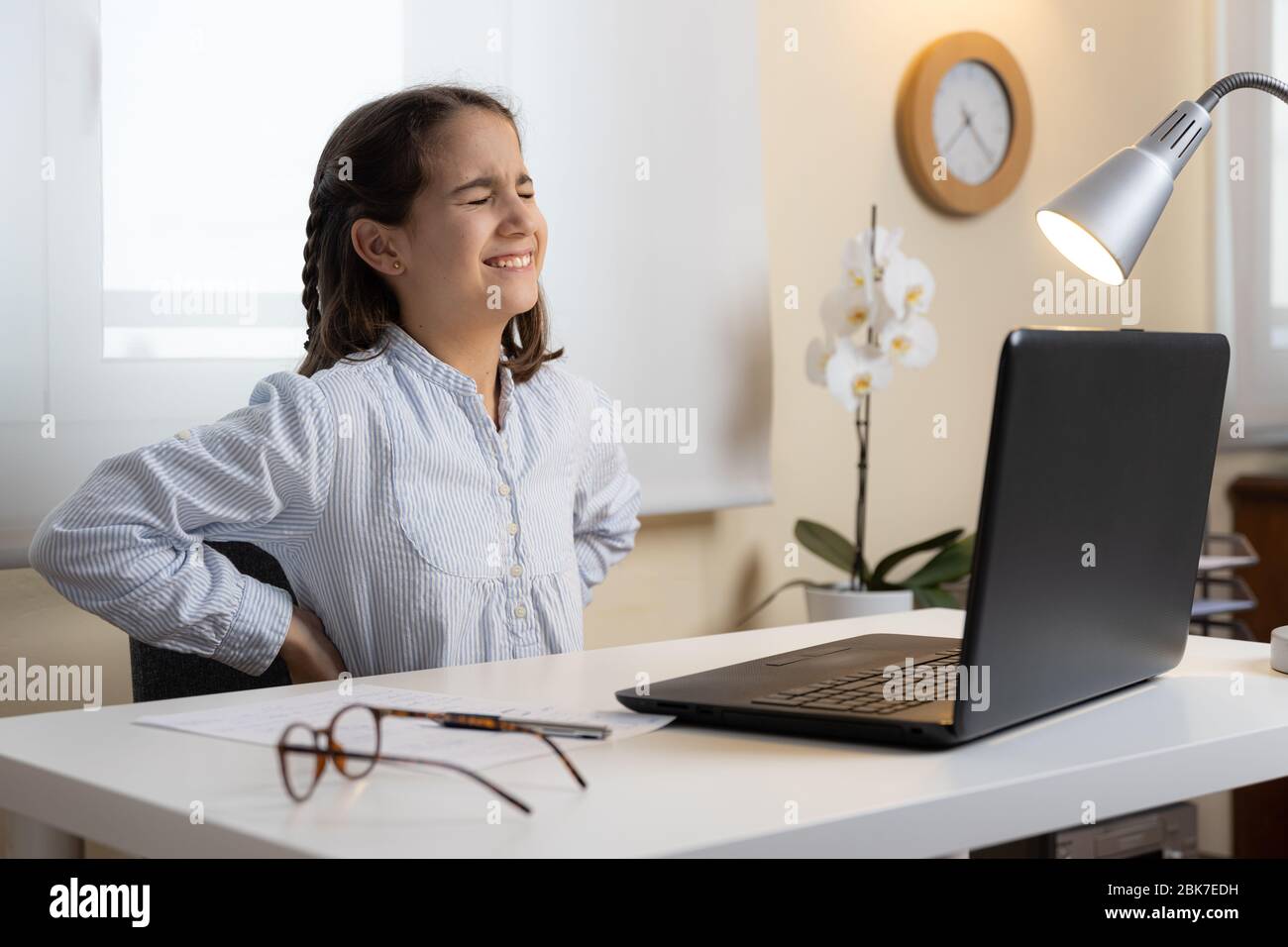 Niña que sufre de dolor de espalda con la computadora en casa Foto de stock
