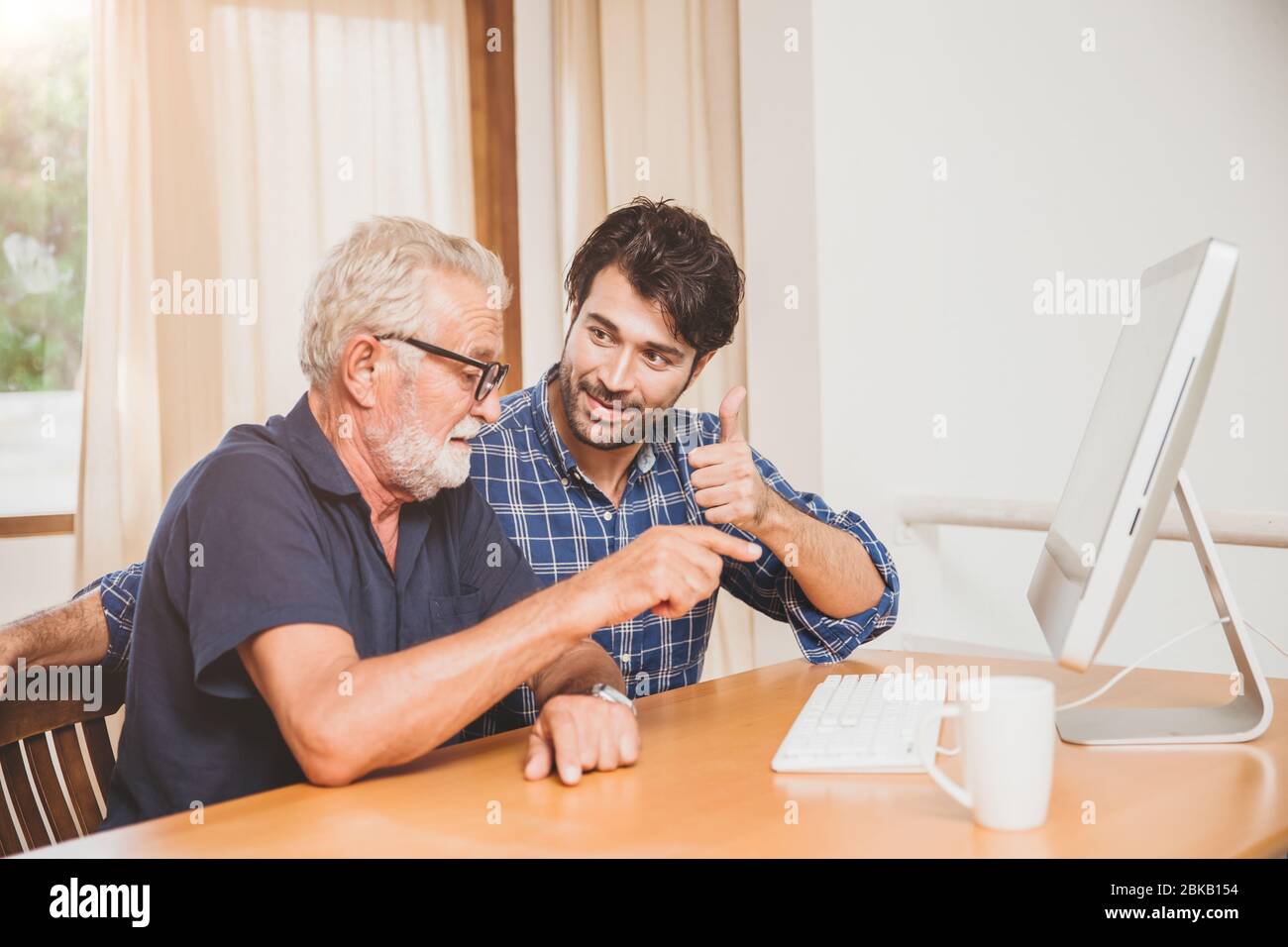 joven o hijo enseñando a su abuelo padre mayor aprender a usar la computadora en casa. Foto de stock