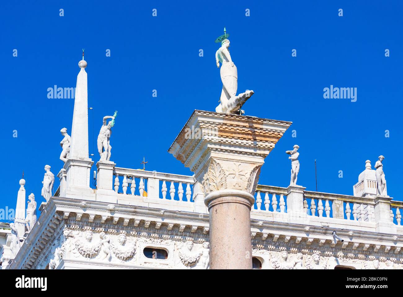 La parte superior del edificio Biblioteca Nazionale Marciana y la parte superior de la columna de granito que lleva uno de los símbolos de Venecia-San Teodoro en la Piazza San Marco Foto de stock