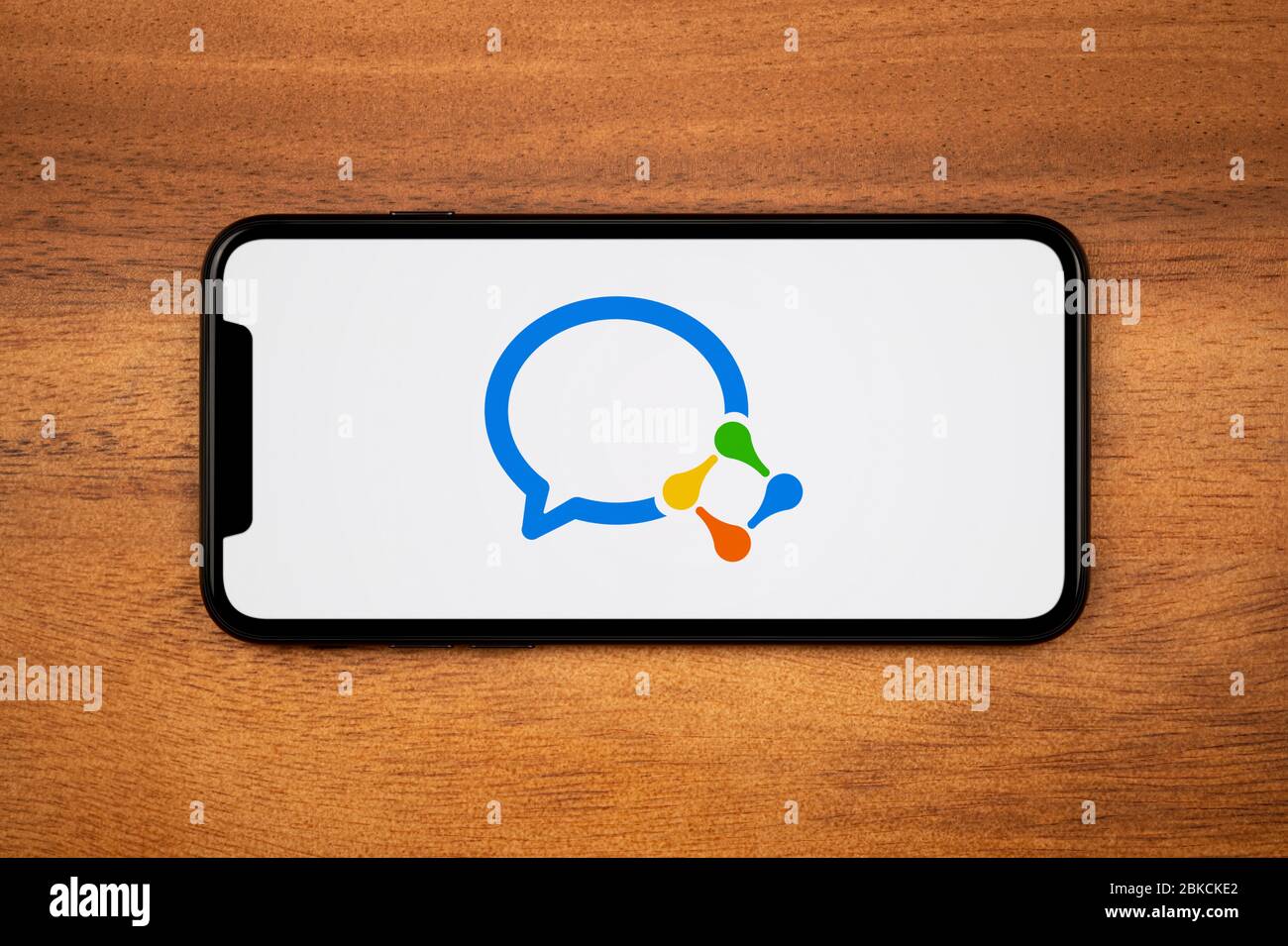 Un smartphone que muestra el logotipo de trabajo de WeChat descansa sobre una mesa de madera plana (sólo para uso editorial). Foto de stock