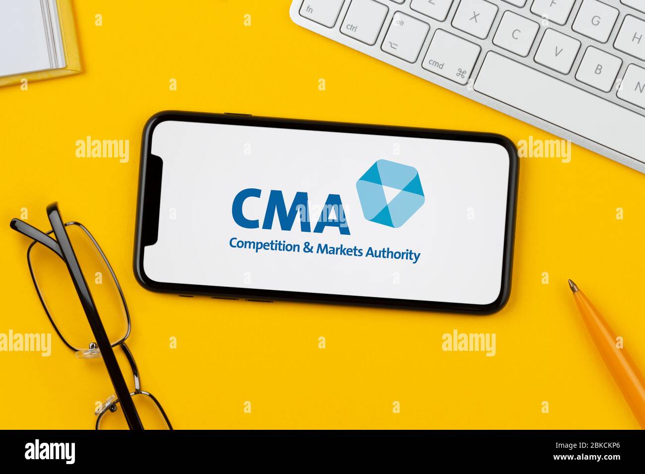 Un smartphone que muestra el logotipo CMA (autoridad de competencia y mercados) se apoya en un fondo amarillo (sólo para uso editorial). Foto de stock