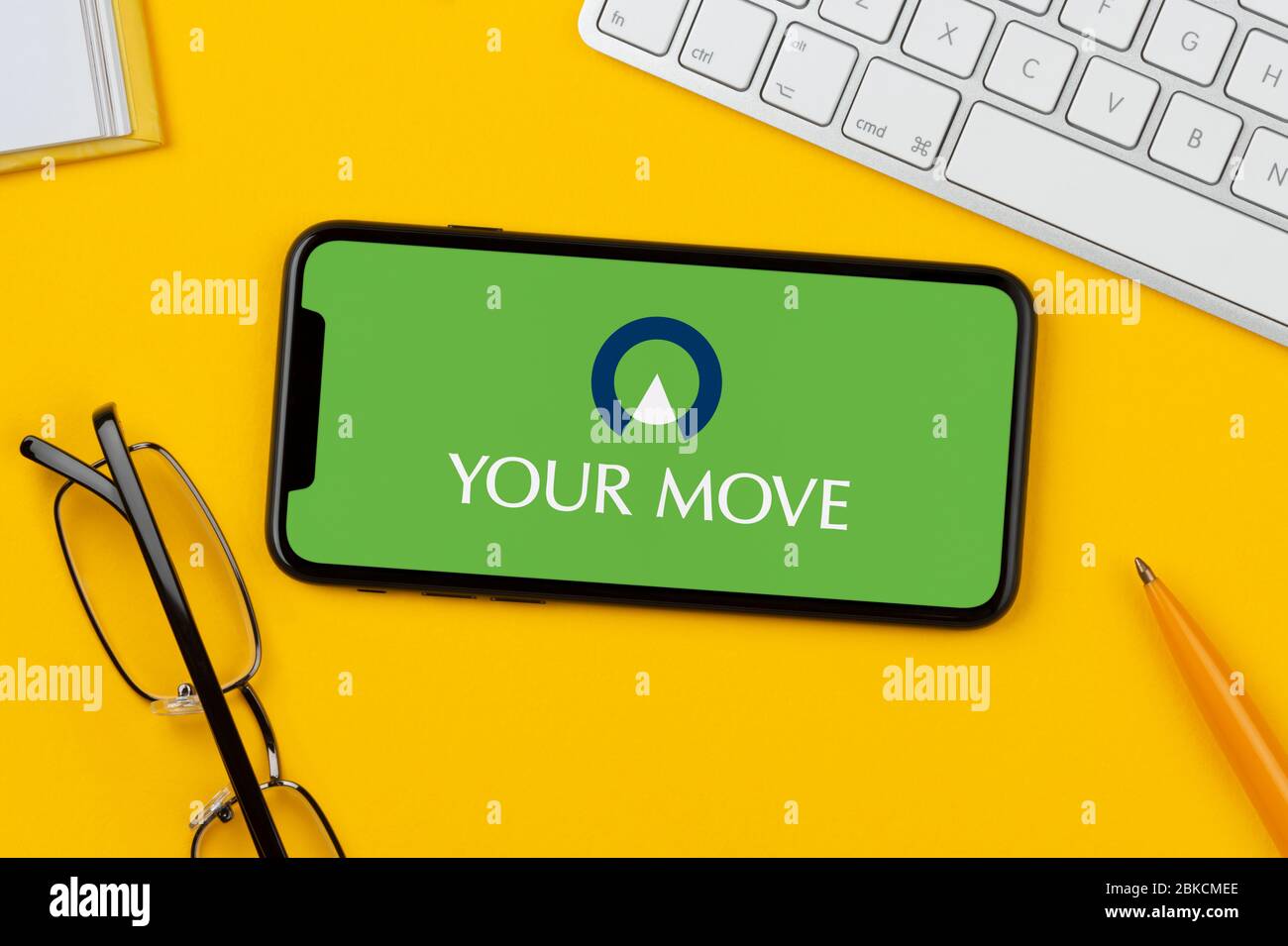 Un smartphone que muestra el logotipo de su movimiento se apoya sobre un fondo amarillo junto con un teclado, gafas, lápiz y libro (sólo para uso editorial). Foto de stock