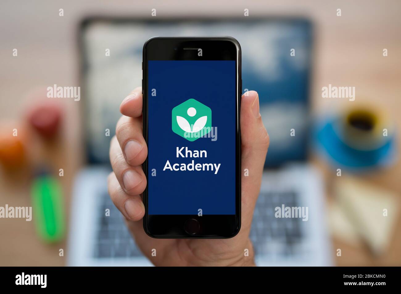 Un hombre mira su iPhone que muestra el logotipo de Khan Academy (sólo para uso editorial). Foto de stock