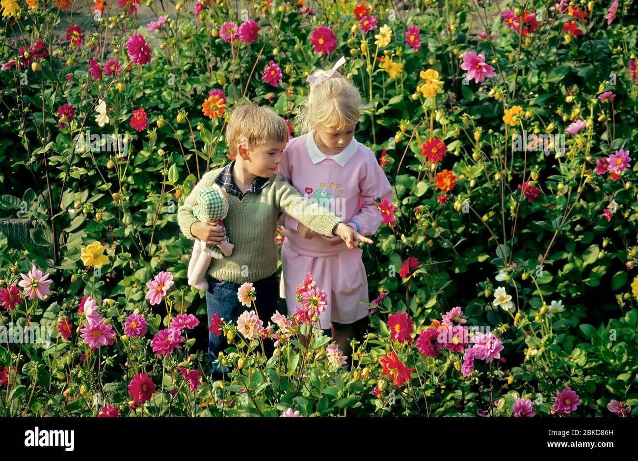 Niño y niña en jardín de flores con muñeco de tela Foto de stock