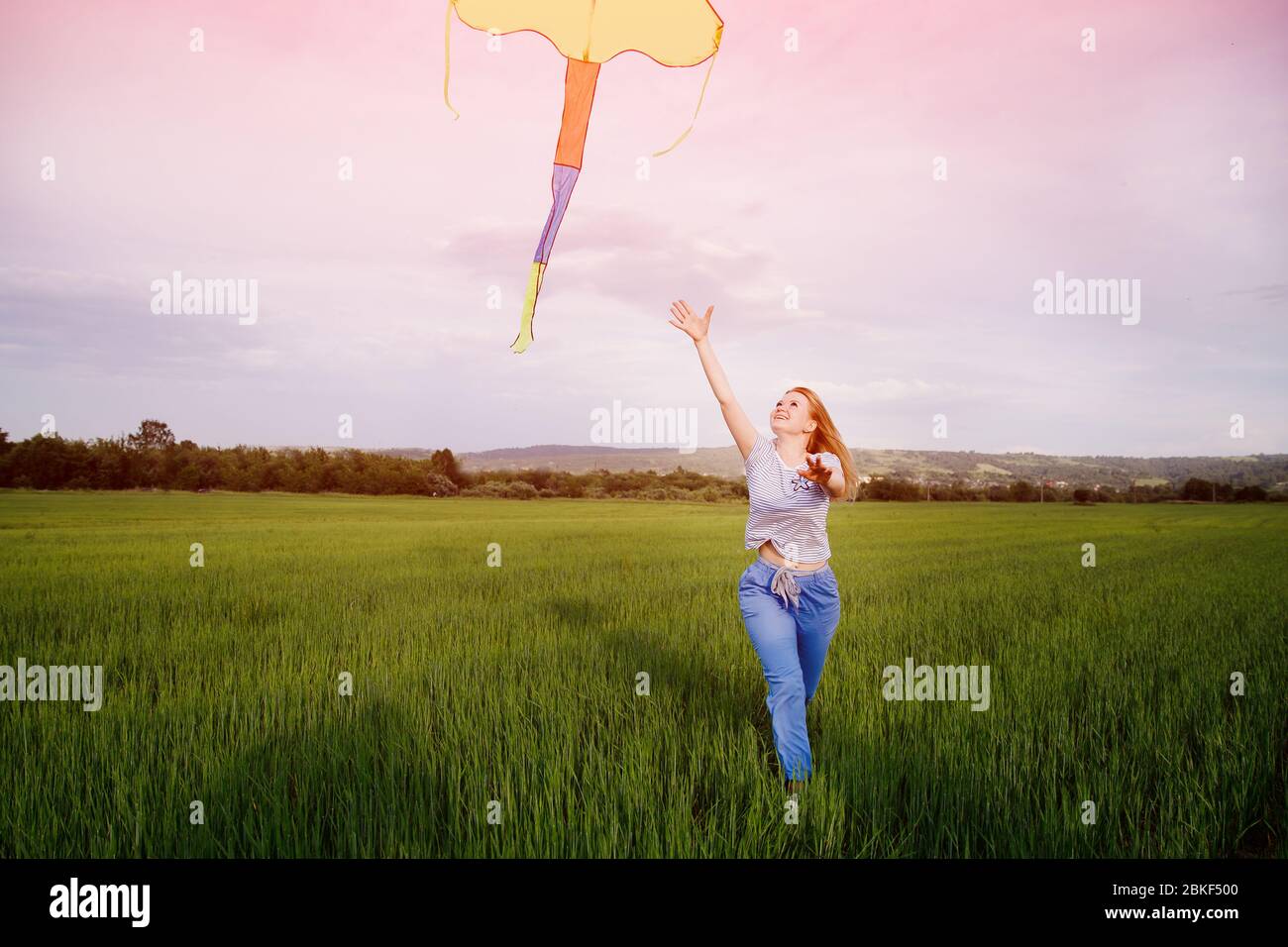 Una joven corre con cometa a través de un campo limpio al atardecer, el viento sopla su cabello. Concepto de libertad de grilletes, juicios. Foto de stock