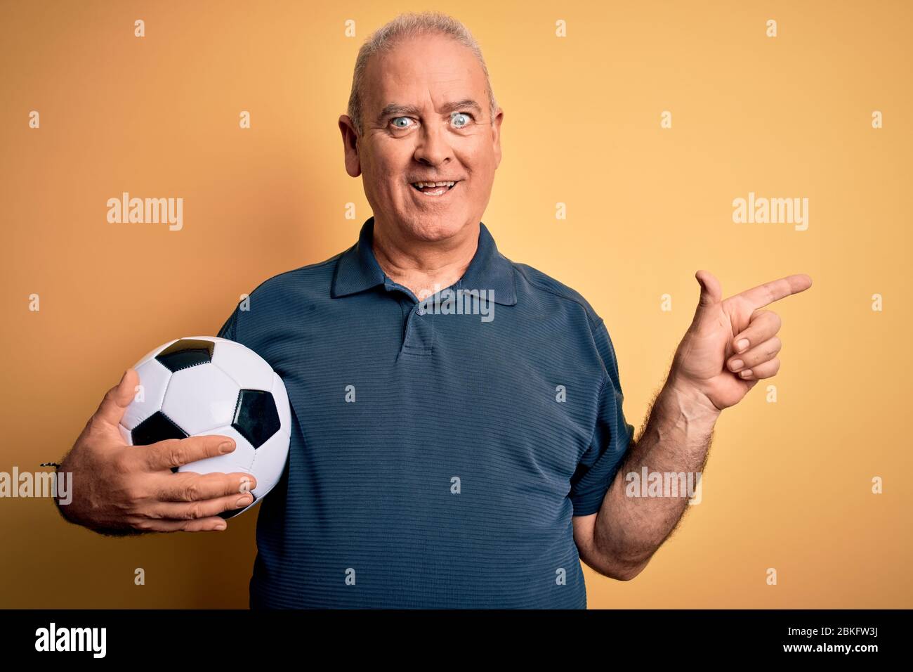 Edad media hoary jugador hombre jugando fútbol sosteniendo la pelota de  fútbol sobre fondo amarillo muy feliz señalando con la mano y el dedo a un  lado Fotografía de stock - Alamy