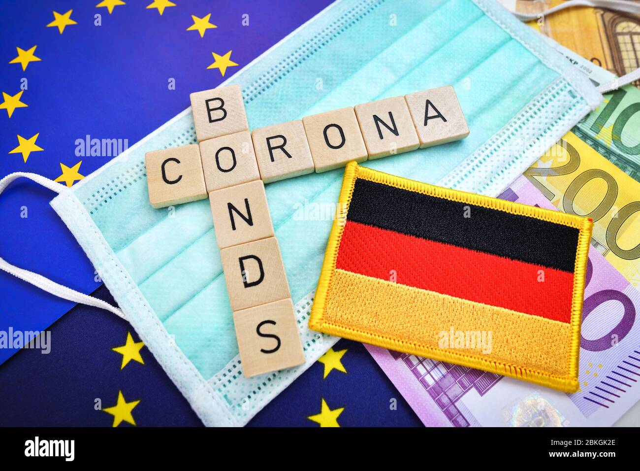 Letras que deletrea la palabra corona Bonds en el lutorio con la bandera de la UE y Alemania / Buchstaben bilden Schriftzug Corona-Bonds auf Mundschutz mit EU- Foto de stock
