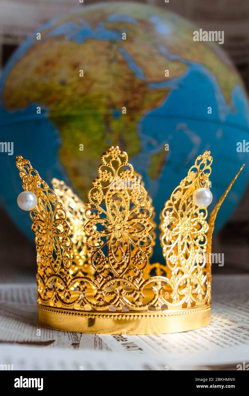 Corona de oro con perlas que representan a Covid-19 en periódicos con globo sobre fondo bokeh. Foto de stock