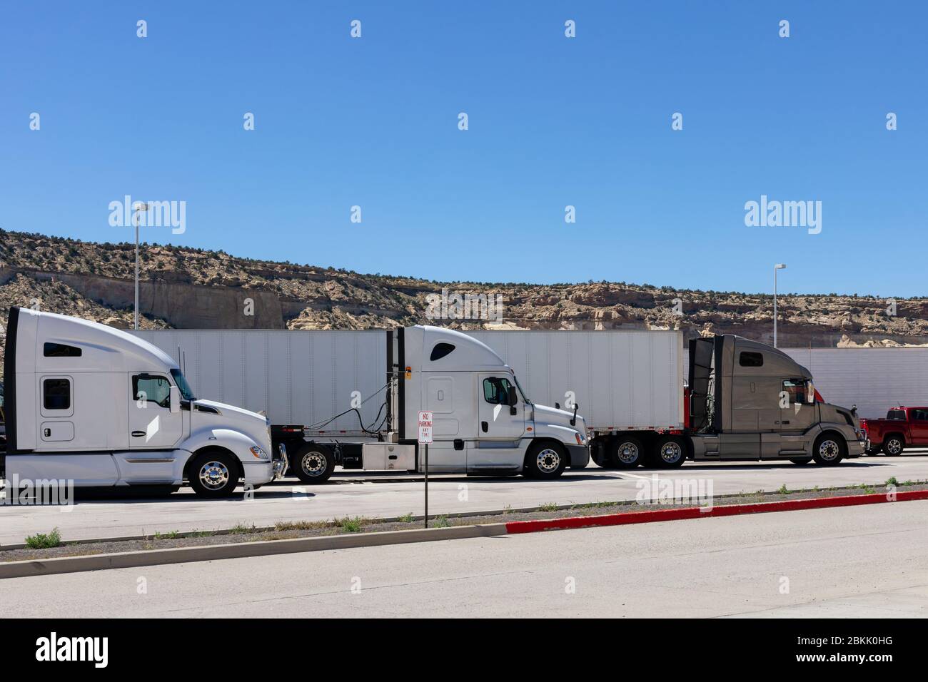 Tres grandes plataformas semi camiones de diferentes marcas modelos están alineados en aparcamientos paradas de camiones o áreas de descanso que llenan los lugares vacíos para descansar y almorzar Foto de stock