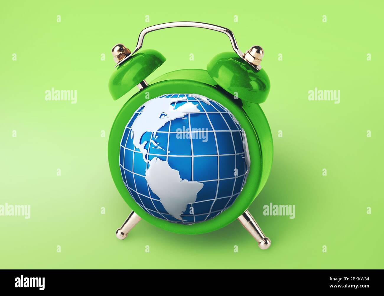 Concepto de tiempo mundial. Reloj de alarma con el planeta Tierra en lugar de reloj de arena sobre fondo verde, collage Foto de stock
