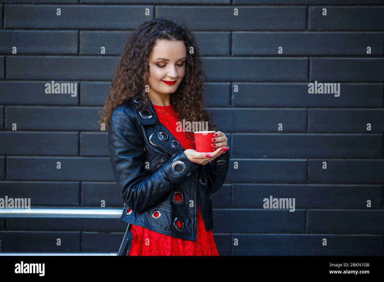 Una niña con un vestido rojo y una chaqueta negra bebe café de una taza de  papel rojo Fotografía de stock - Alamy