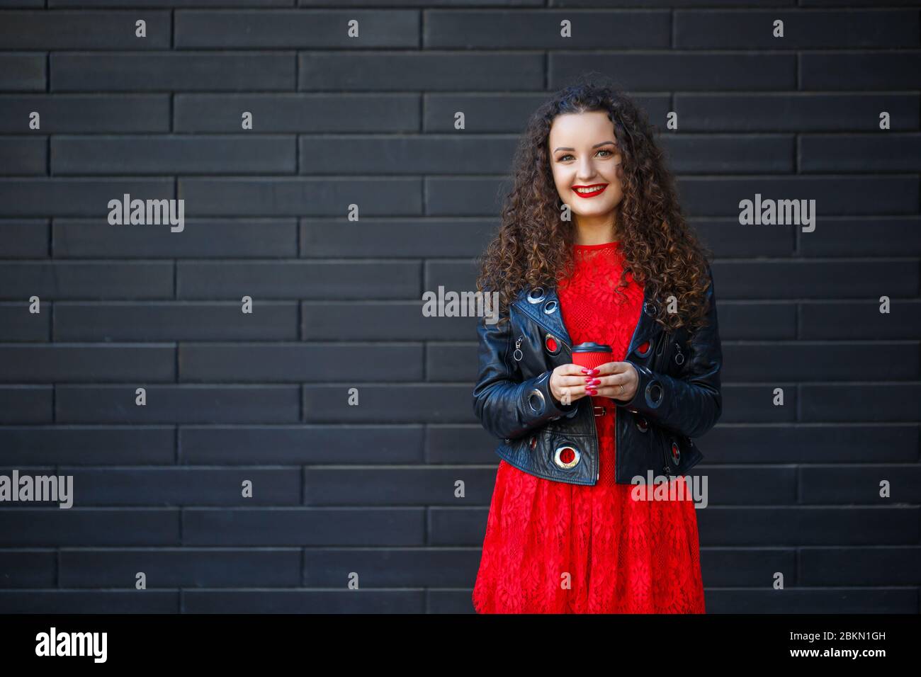 Una niña con un vestido rojo y una chaqueta negra bebe café de una taza de  papel rojo Fotografía de stock - Alamy