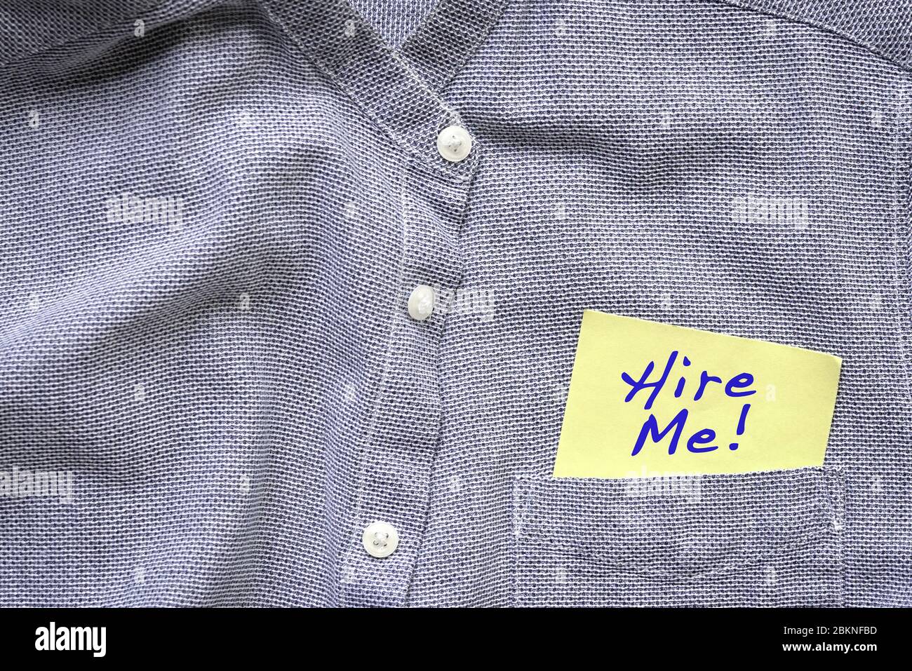 Hire me, palabras en azul sobre un papel amarillo pegado fuera del bolsillo azul gris de la camisa. Concepto de empleo. Foto de stock