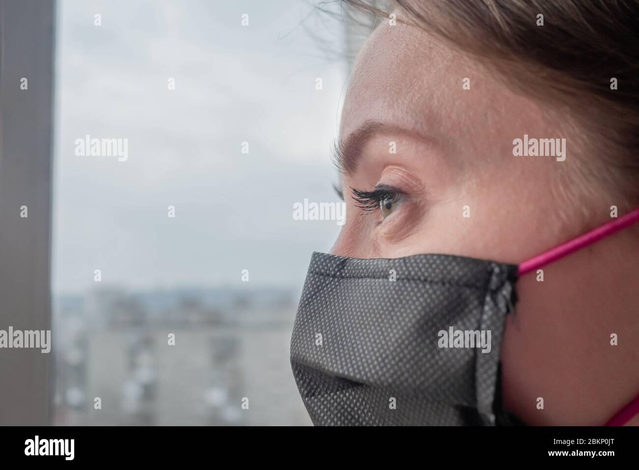 Retrato de una mujer pensativa con mascarilla facial médica negra y mirando por la ventana en casa - primer plano. Aislamiento, prevención, cuarentena Foto de stock