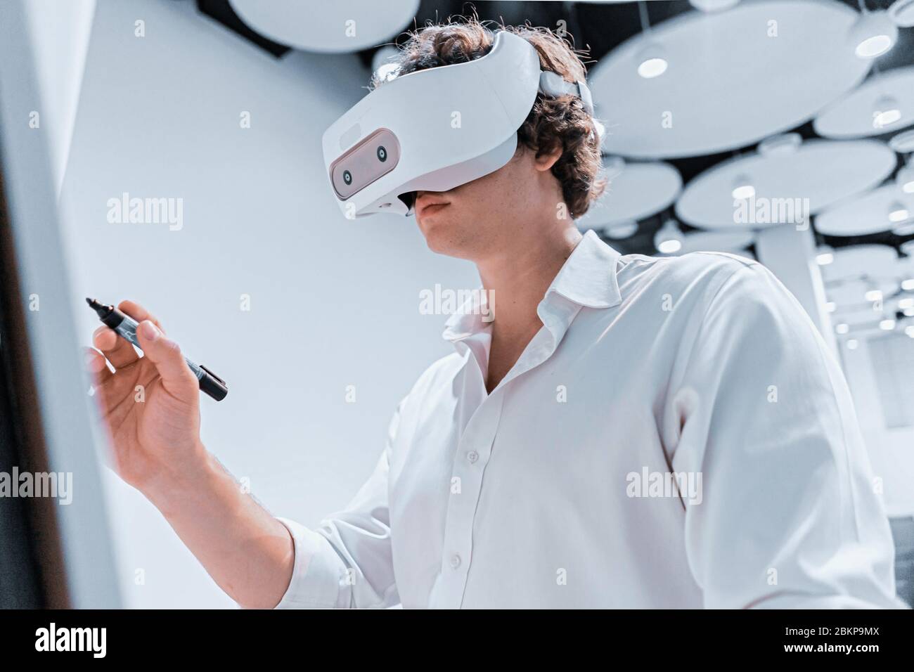 Hombre joven con gafas de realidad Virtual escribiendo en Flipchart durante la presentación en línea en escena sin espectadores. Distanciamiento social. Quédate en casa Foto de stock