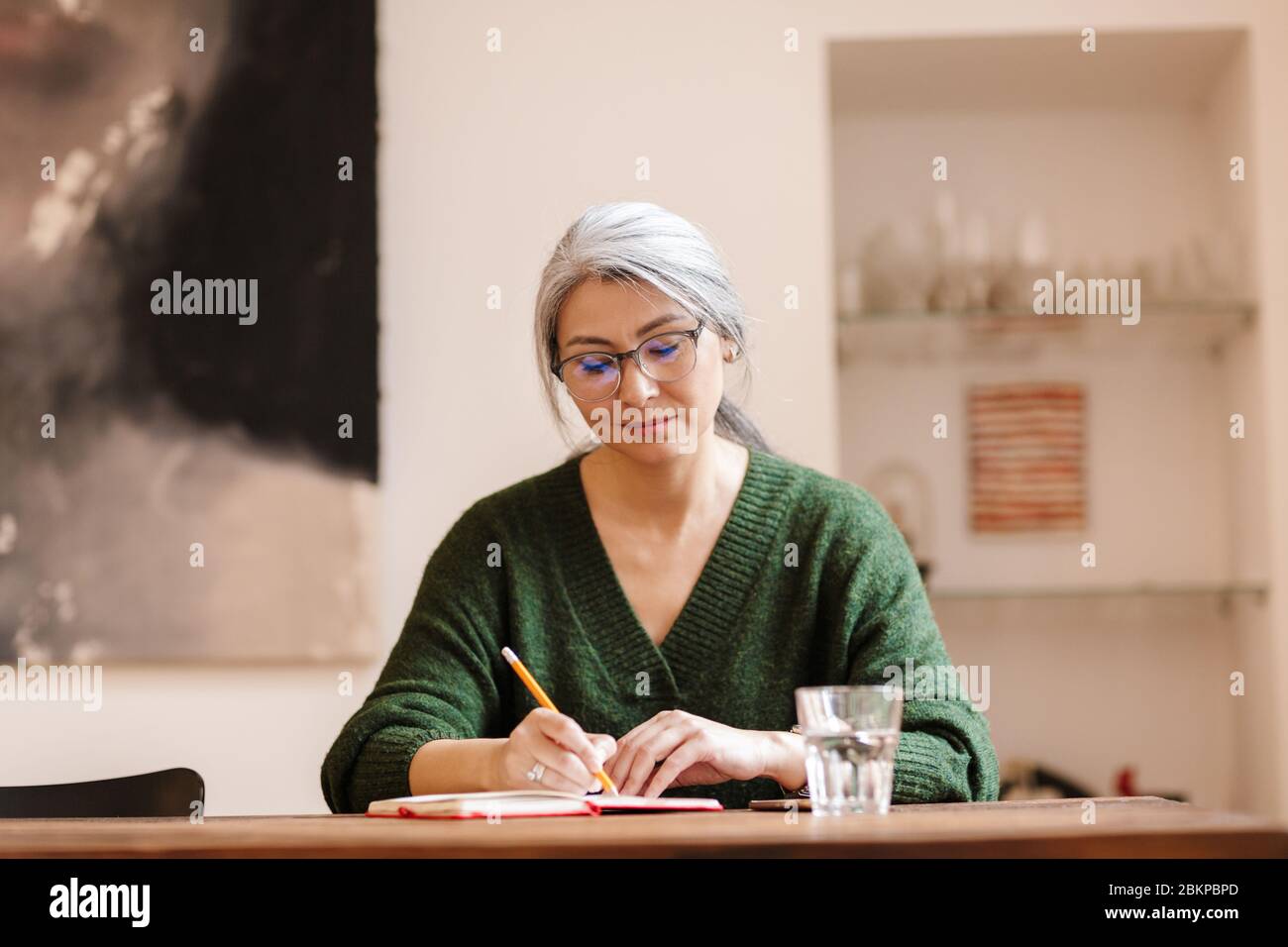 Foto de mujer madura optimista concentrada hermosa de pelo gris en interiores escribir notas. Foto de stock