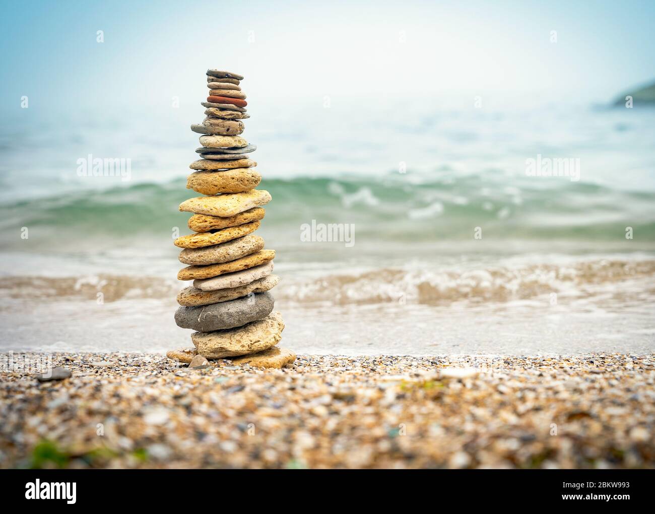 Pirámide de piedras sobre arena que simboliza zen, armonía, equilibrio. Energía positiva. Océano en el fondo Foto de stock