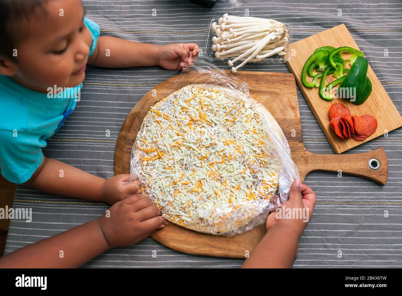 Los niños preparan una pizza de queso congelado con setas enoki, pimientos y pimientos de pavo. Foto de stock