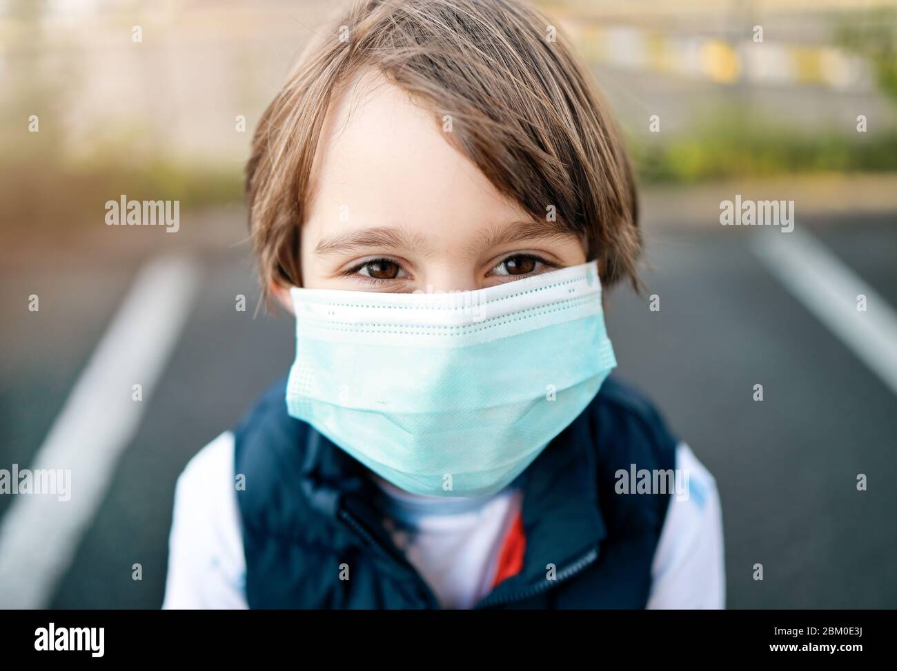 Niño pequeño que lleva máscara médica durante la pandemia de Coronavirus COVID-19. Primer plano y contacto visual con el visor. Regreso a la escuela, Nueva realidad y Prevención Foto de stock