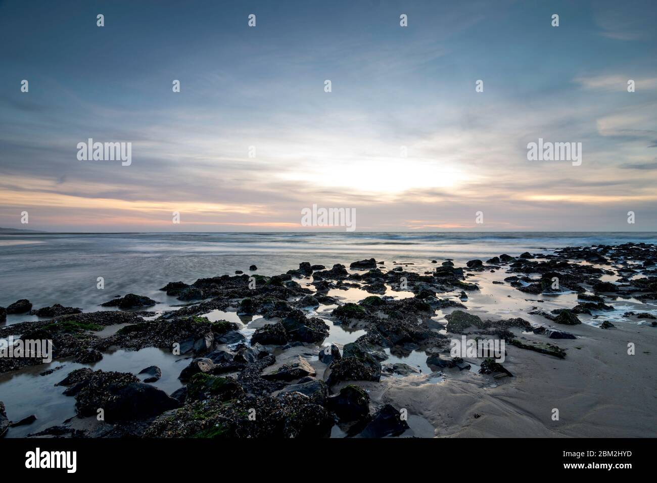 Ambiente nocturno sobre el muelle en el mar. Las piedras reflejan la luz de la noche y los últimos rayos del sol. La arena ondulada se puede ver a través del shal Foto de stock