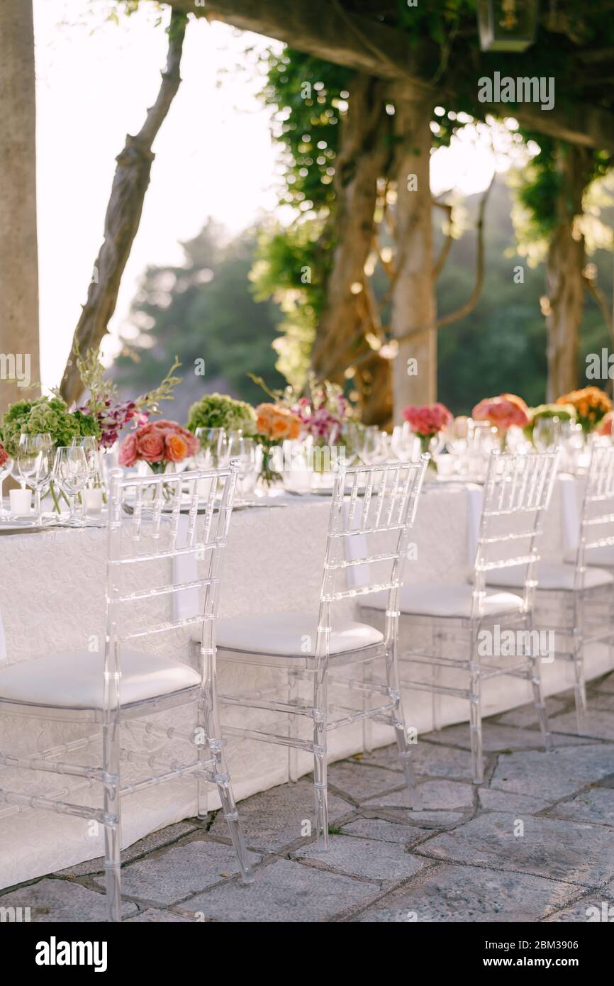 Cena de boda mesa de recepción. Sillas de cristal transparente Chiavari,  Tiffany, se encuentran cerca de la mesa con flores. Contra el fondo de la  luz del atardecer Fotografía de stock -