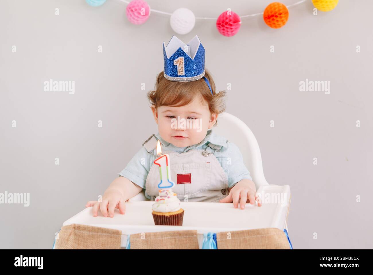 Lindo y adorable bebé caucásico en corona azul celebrando su primer  cumpleaños en casa. Niño niño niño niño pequeño sentado en silla alta  mirando el cupcake dess Fotografía de stock - Alamy