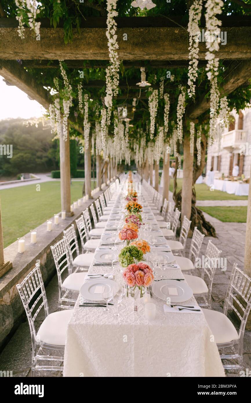 Cena de boda mesa de recepción. Una mesa muy larga para los huéspedes con  mantel blanco, arreglos florales, sillas transparentes de plástico de  cristal Chiavari Fotografía de stock - Alamy