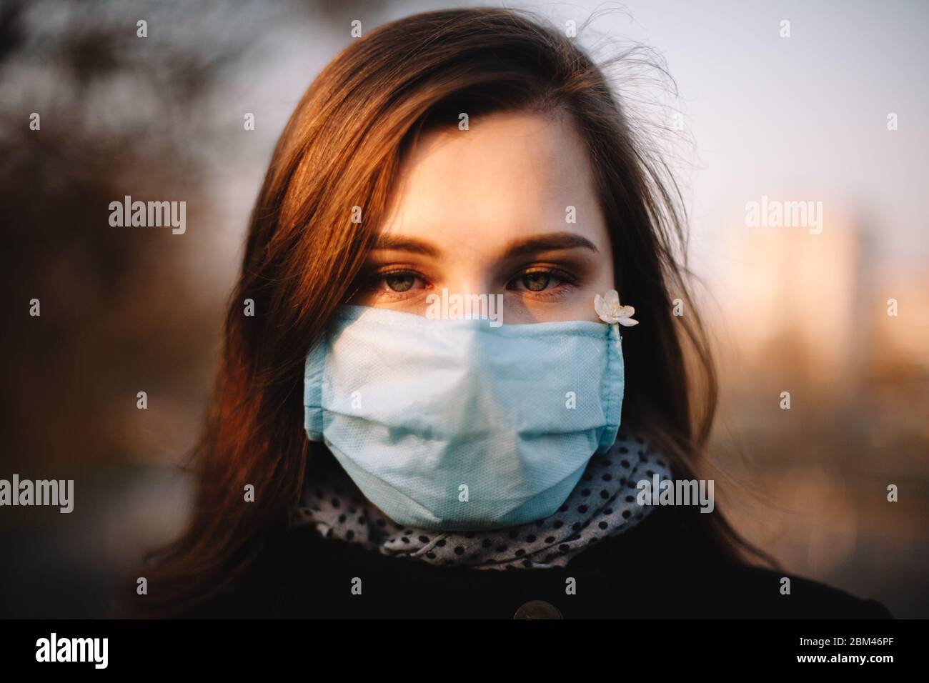 Retrato de cerca de una adolescente enferma triste usando máscara médica de protección facial parándose al aire libre en el parque durante la primavera Foto de stock