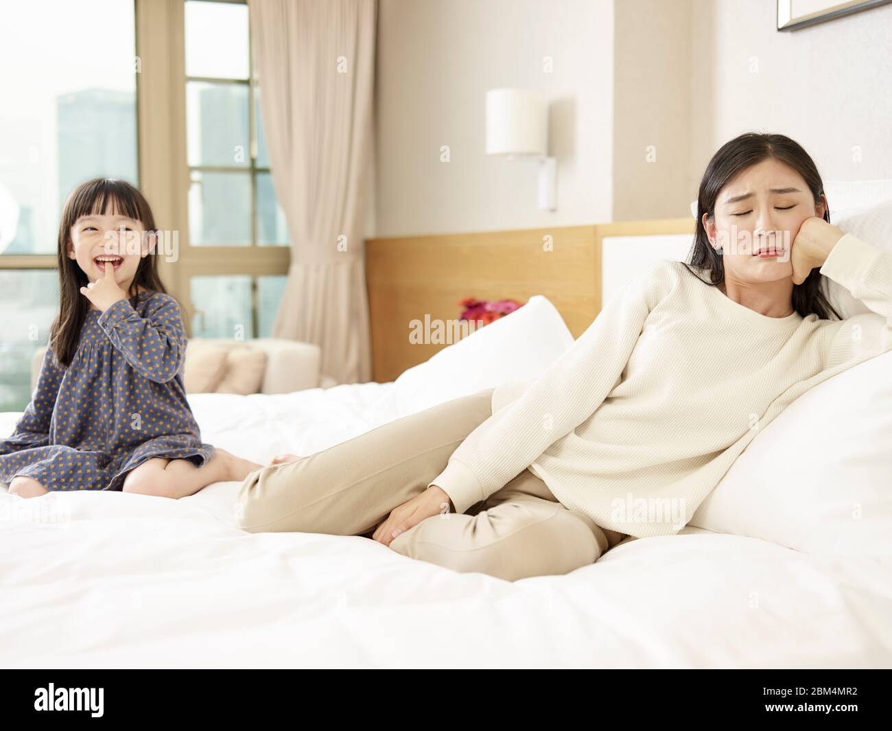 joven madre asiática fingiendo ser infeliz mientras que linda hija riendo Foto de stock
