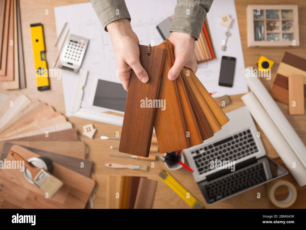 Diseñador de interiores profesional mantiene muestras de madera para la placa base y el rodapié, manos de cerca con el fondo de escritorio Foto de stock