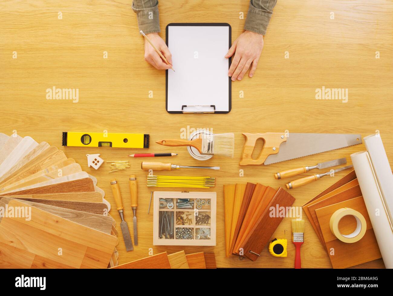 Hombre manos bosquejando un proyecto en un portapapeles, mesa de trabajo con herramientas de bricolaje vista superior Foto de stock