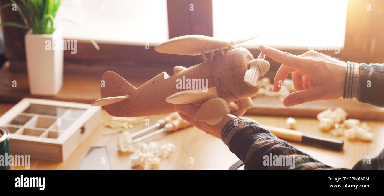 Hombre jugando con un propulsor de avión de juguete de madera con herramientas y virutas en el fondo, bricolaje y hobby concepto Foto de stock