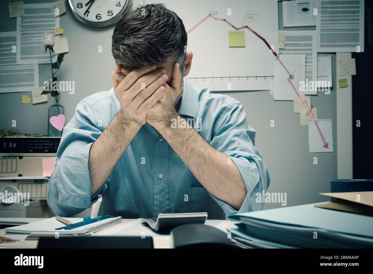 Trabajador de oficina desesperado con la cabeza en las manos y gráfico financiero negativo en el fondo. Foto de stock