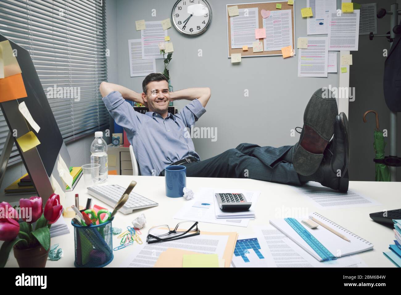 Un trabajador de oficina perezoso se relaja en su pequeña oficina. Foto de stock