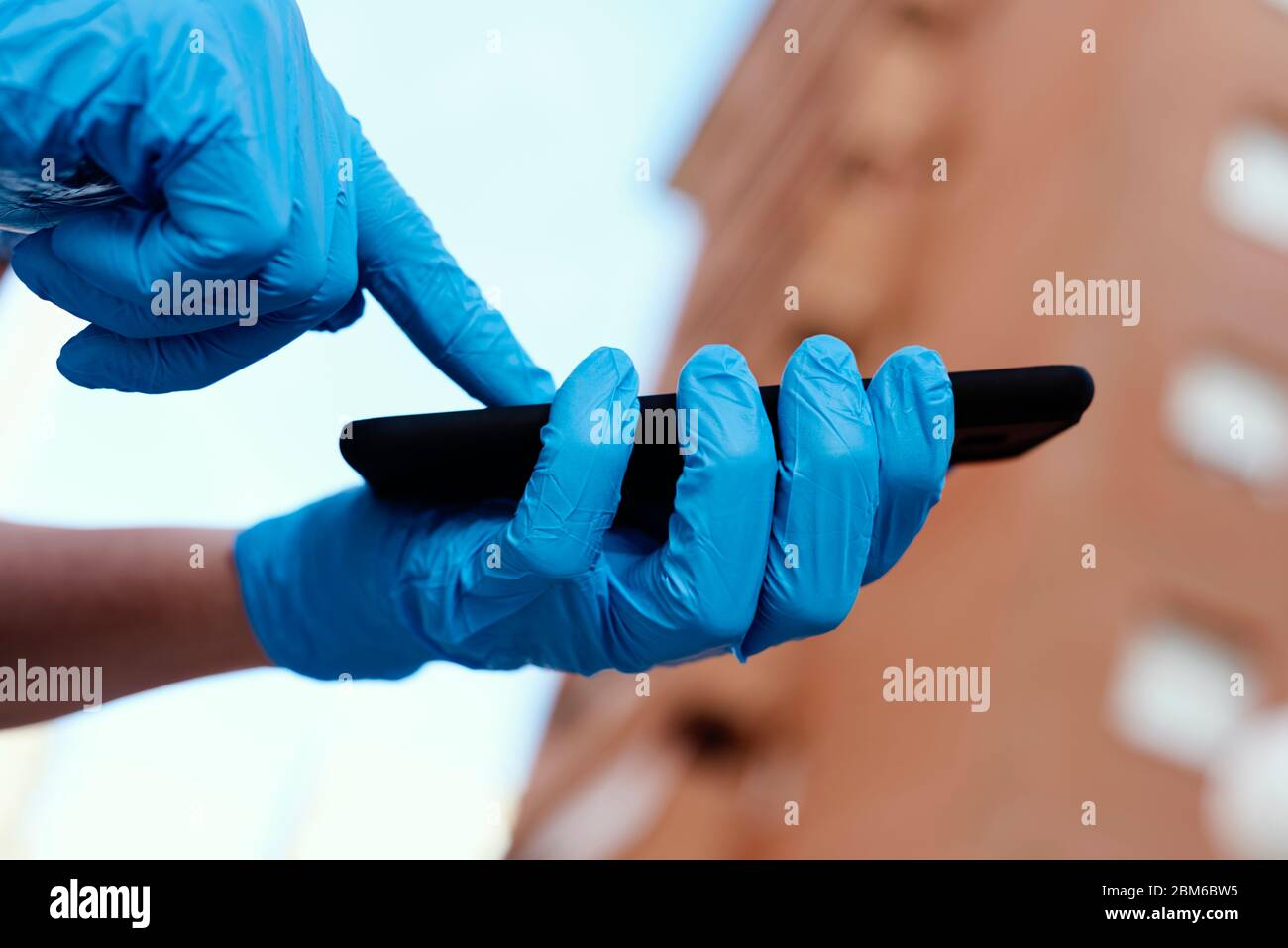primer plano de un joven caucásico en la calle, con guantes de látex azul, usando su smartphone Foto de stock