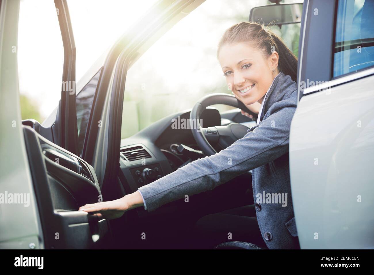 Joven mujer atractiva apertura puerta de coche tras aparcar y sonriendo a la cámara. Foto de stock