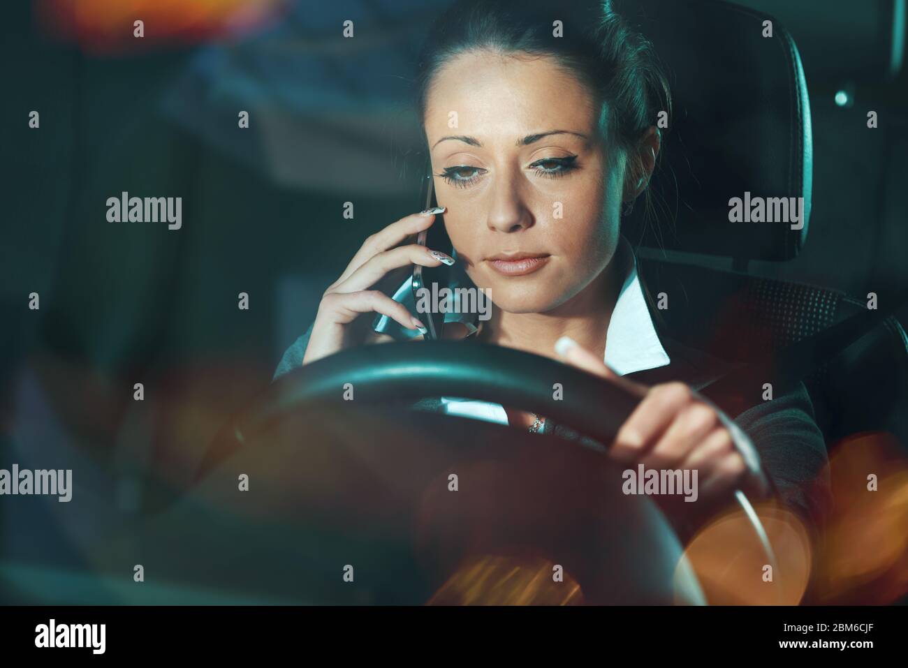 Mujer cansada distraída llamando mientras conduce tarde por la noche. Foto de stock