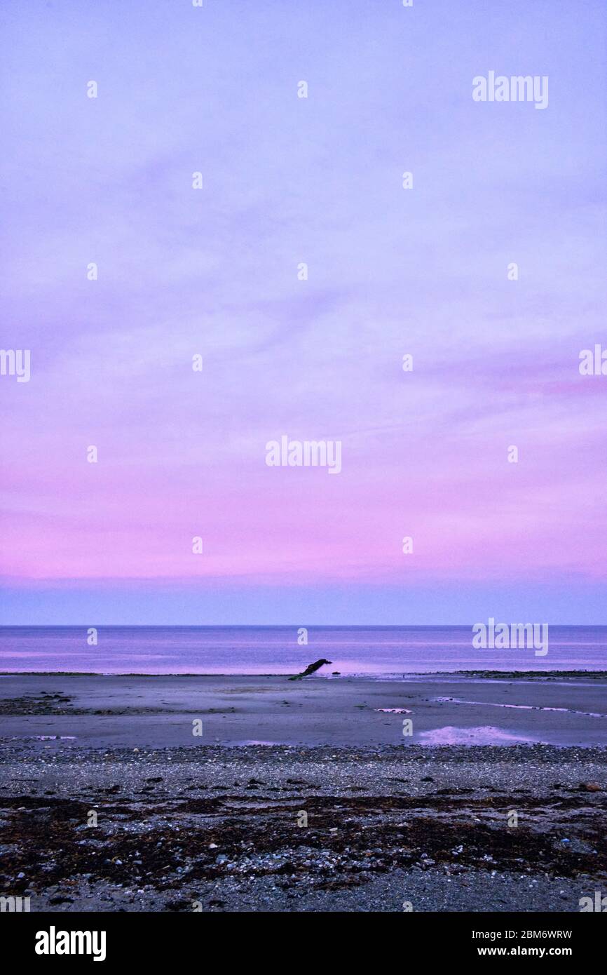 Vista de poca luz en la costa este de la Isla de Man al atardecer con colores rosas al cielo y la playa Foto de stock