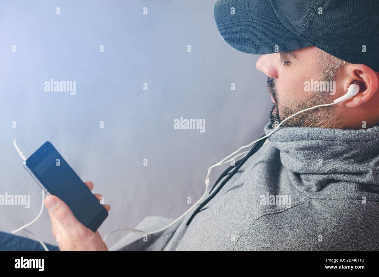 Retrato recortado de un hombre con barba en negro, viendo vídeos o escuchando música con los auriculares del smartphone. Espacio de copia Foto de stock