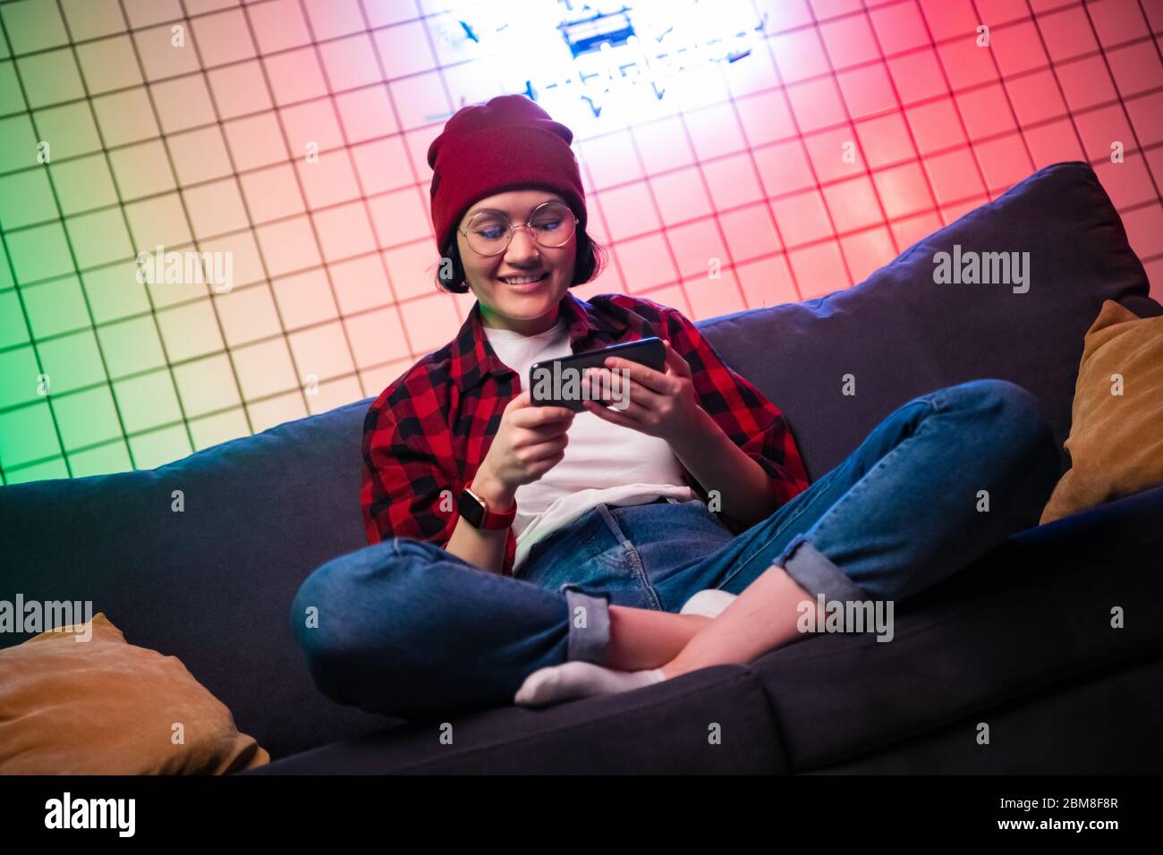 Niña adolescente sosteniendo un smartphone mientras juega a juegos de disparos en línea. Gesto de pulgares arriba. Foto de stock