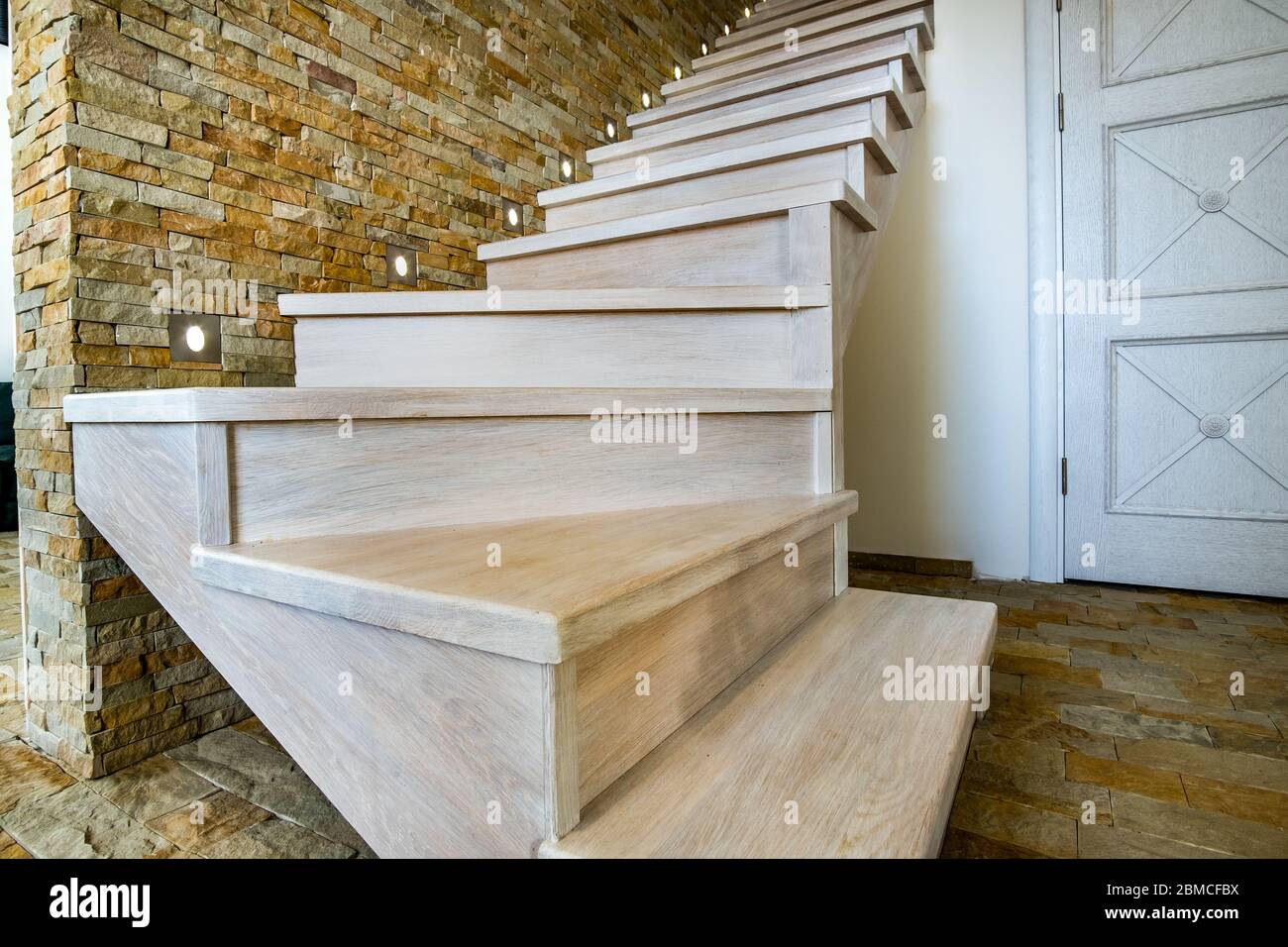 Elegante escalera contemporánea de madera en el interior de la casa loft. Pasillo moderno con paredes decorativas de ladrillo de piedra caliza y escaleras de roble blanco. Foto de stock