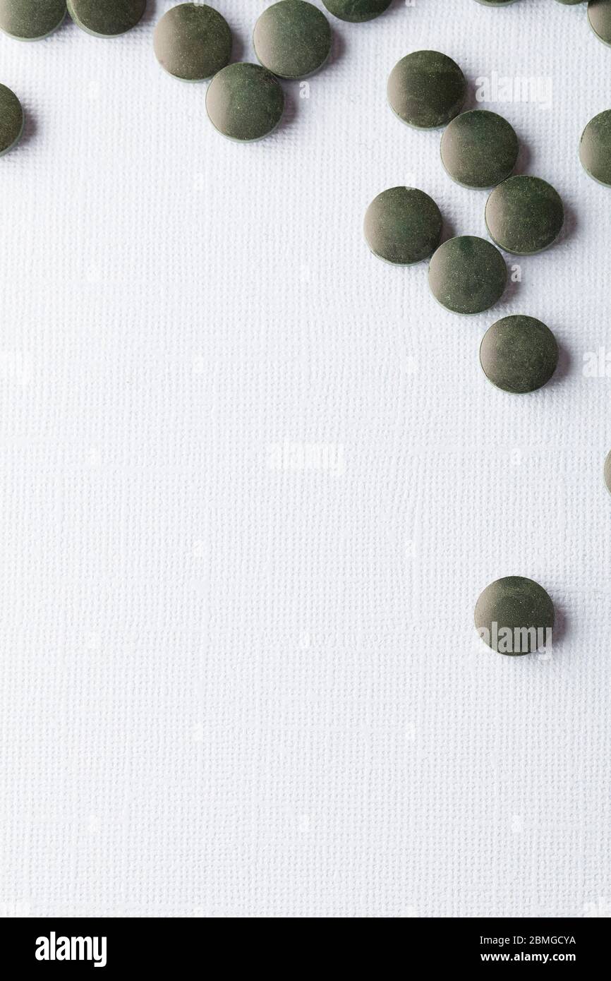 tabletas redondas verdes de espirulina sobre fondo blanco para cerrar el espacio de copia vertical Foto de stock