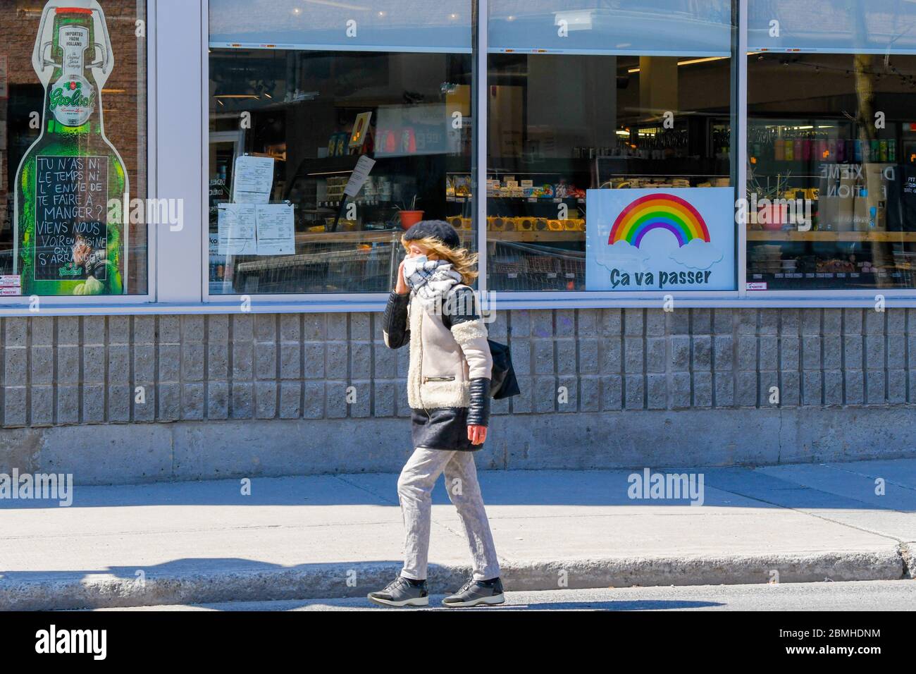 Persona que lleva una máscara protectora y una bufanda que camina delante de una tienda con un covid 19 arco iris de esperanza en ella (el cartel dice en francés: Pasará) , Montreal Canadá Foto de stock