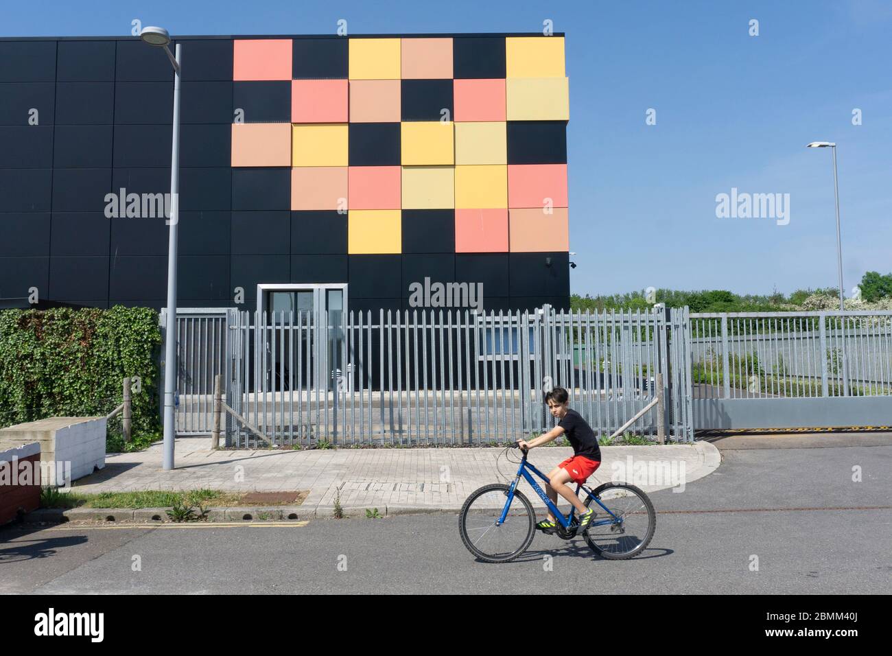 Edificio cúbico negro mate con azulejos amarillos y rojos en una esquina como diseño gráfico detrás de barandillas de seguridad de metal centro de datos de cielo azul intenso Foto de stock
