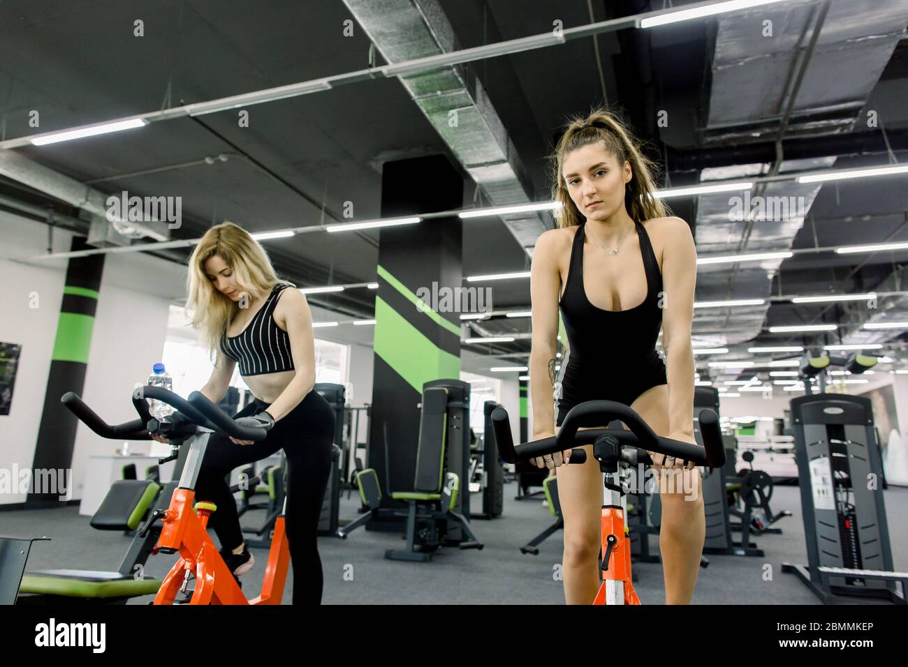 Vista completa de dos chicas jóvenes deportiva haciendo girar en un gimnasio vacío. Dos mujeres haciendo ejercicio en bicicleta en el gimnasio Fotografía de -