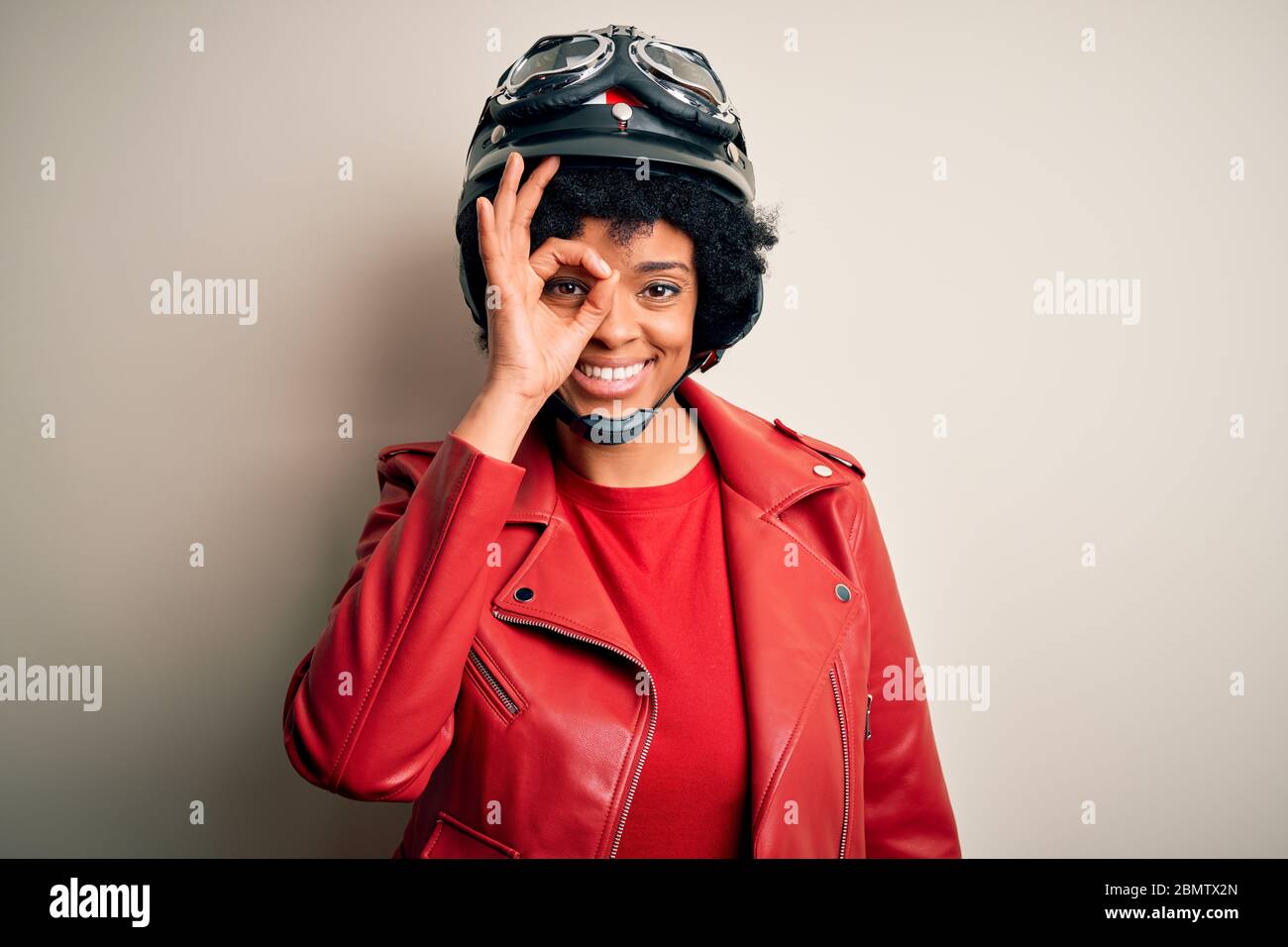 Joven afro americana mujer motociclista con pelo rizado usando casco de  motocicleta haciendo un gesto de ok con la mano sonriendo, ojo mirando a  través de finge Fotografía de stock - Alamy